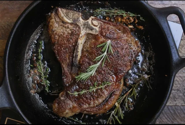 A T-bone steak seared in a cast-iron skillet with rosemary and thyme